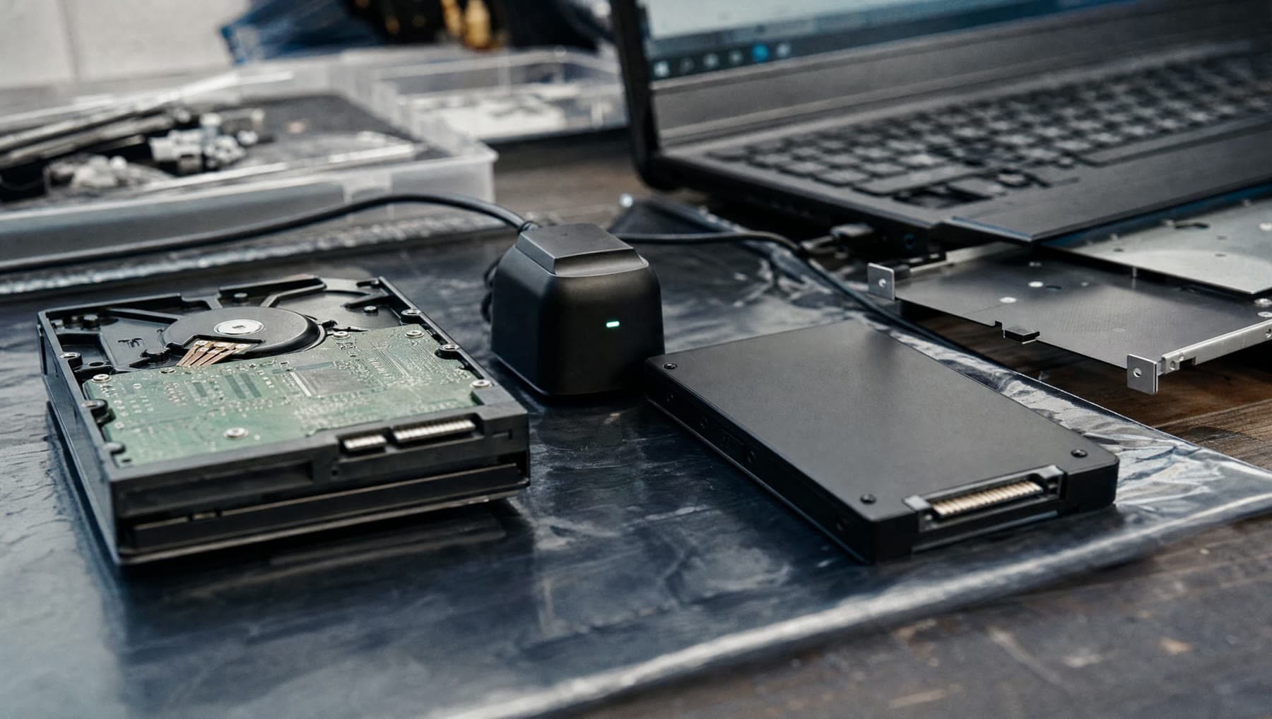 An old spinning hard disk beside a new solid-state drive on an anti-static mat, a cloning dock between them.